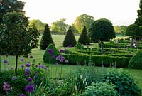 Parterre de haies de buis contenant des baies standard, plantées de santolina et d'Allium 'Purple Sensation' avec des pyramides d'ifs et une pelouse s'étendant vers un ha ha et la campagne du Dorset au-delà. Ancien presbytère, Pulham, Dorset, UK