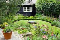 Vue depuis la terrasse en bois surélevée à travers le parterre de fleurs, la pelouse et la maison - Brook Hall Cottages, Essex NGS