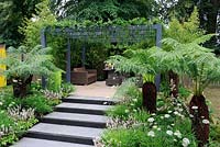 Plantation luxuriante le long des marches du jardin menant à un coin salon et cuisine avec une pergola vivante plantée de fougères et de plantes traînantes. Live Outdoors, Hampton Court Palace flower show 2012