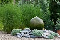 Soutenu par un groupe de Miscanthus, caractéristique de l'eau d'une sphère de granit et de bardeaux plantés avec Artemisia schmidtiana 'Nana' et Miscanthus sinensis