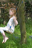 Fille sur une balançoire dans un bois avec Hyacinthoides non-scripta - Bluebells anglais fin avril