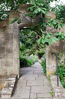 Gravetye Manor en été. Entrée de jardin en pierre masquée de Magnolia campbellii.
