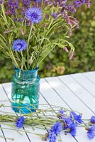 Arranger Centaurea cyanus - Bleuet avec Salvia nemorosa 'Ostfriesland' dans un vase en verre bleu