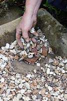 Planter un évier en pierre alpine - remplir le trou de drainage avec des pots et une couche de bardeaux de pois. Répartissez les pots sur la base pour le drainage