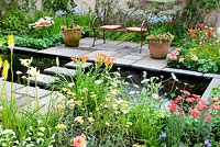 Parterres de fleurs et pots avec plantation herbacée mixte et piscine centrale avec tremplins menant à un coin salon intime dans le jardin 'Summer Fairytale'. RHS Tatton Flower Show 2013