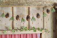 Étape par étape de faire une guirlande de Noël simple et rustique avec des pommes de pin et des aiguilles de pin - La guirlande finie accrochée à une porte en bois