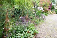 Plantation à la fin de l'été autour de supports de plantes décoratives, y compris Phlox, Salvia, Fenouil, Cotinus et roulotte gitane en arrière-plan
