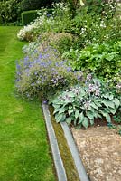 Une simple rigole longe le parterre de fleurs herbacées, y compris des hostas glauques et des géraniums.
