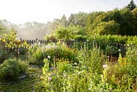 Jardin aux herbes de style naturel avec clôture en bois et sphère en verre. Plantation, Borago officinalis, Calendula officinalis, Papaver somniferum