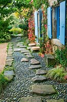 Jardin de style japonais - vue sur le côté est de la maison avec volets bleus, chemin avec galets et rochers et jardin de gravier
