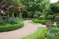 Jardin de campagne formel avec des chemins de gravier à travers des parterres de fleurs en forme de topiaire avec une couverture de Buxus basse, des alliums et de l'aubépine rose