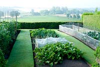 Jardin potager avec des bordures de légumes contenant de la betterave, des carottes - poussant sous une toison protectrice - et des oignons, des haricots et du chou avec vue rurale sur Cheshire au-delà