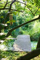 Chemin menant sur un pont en bois, étang dans le jardin avec bambou et carillons éoliens dans l'arbre