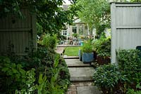 Jardin de la ville avec parterres surélevés, jardinières peintes en bleu, pelouse, chemin en pierre et en brique menant à une véranda.