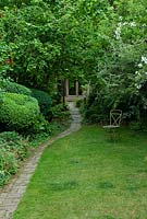 Jardin de la ville, chemin en briques serpentant vers le studio de jardin, parterres de fleurs avec des arbustes, des arbres et des vivaces, y compris Buxus - boîte et géraniums rustiques.