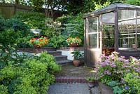 Vue sur le jardin avec Spirea 'Candlelight' Nasturtium 'Firebird' en pot en terre cuite, siège de jardin et serre hexagonale
