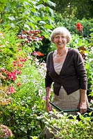Portrait du propriétaire de Janet Daniel arrosant son jardin. Les plantes comprennent le fuchsia, l'aster et l'anémone japonaise