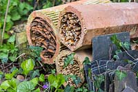 Tuyaux en terre cuite remplis d'une variété de matériaux de nidification pour les insectes, dans un parterre de jardin