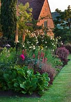 Parterre de fleurs rouges avec Rosa, Eremurus, Bergenia 'Eric Mmith', Rosa 'Buff Beauty' et Eremurus 'Cleopatra '. Sandhill Farm House, Hampshire