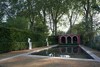 Vue sur piscine sereine avec haies taillées, sculpture et loggia. Plantation douce sur le côté opposé. Le jardin Renaissance BrandAlley.