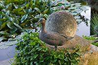 L'étang aux nénuphars depuis la terrasse en gravier à côté de la maison - sculpture de canard et boule de pierre. Les Confines, Provence, France