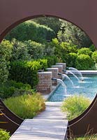 Jardin contemporain moderne - cercle 'oculus' en métal et piscine au-delà avec quatre jets d'eau en brique