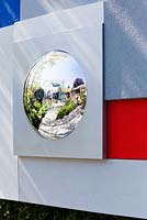 Détail d'un miroir circulaire déformant fixé au mur avec des panneaux de bleu et de rouge, The Mind's Eye garden pour le RNIB, médaillé d'or. RHS Chelsea Flower Show 2014.