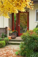 Jardin d'entrée d'automne avec porte rouge, chemin, pots avec décor d'automne. Nandina domestica - Bambou céleste, Acer palmatum - Érable japonais.