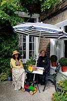 Deux femmes assises à une table sous un parasol dans un jardin ouvert sous le National Garden Scheme NGS dans le London Borough of Hackney et vendant des billets pour l'événement.
