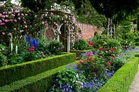 Un jardin clos anglais classique avec des parterres de fleurs ornementaux à bords arrondis, des rosiers grimpants et une tonnelle décorative en bois - Seend, Wiltshire