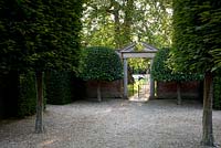 Vue depuis la grande allée de style français à la porte formelle dans le jardin clos avec fronton en pierre et arbres topiaires jumeaux de chaque côté. Seend, Wiltshire