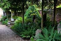 Jardin à feuillage vert avec un siège en pierre devant une pyramide couverte de lierre tous sous des arbres à baldaquin surélevé - Seend, Wiltshire