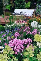 Un jardin Hampton. Parterres de fleurs colorés, plan d'eau, terrasse en bois surélevée, banc en bois