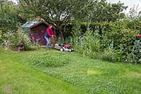 Création d'un monticule de trèfle - Femme tondant la pelouse dans son jardin arrière.