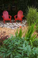 Deux chaises Adirondack en bois rouge sur patio dallé à côté de Miscanthus sinensis 'Strictus', Paeonia lactiflora au premier plan et Berberis thunbergii dans le jardin en été, sous le jardin des pommiers, Canada