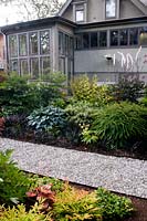 Chemin de gravier menant à travers des parterres d'été, avec vue sur l'extérieur de la maison. Hosta, Ophiopogon, fougère. Victoria BC, Canada