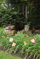 Hemerocallis - hémérocalles, nichoir en céramique sur des rochers empilés et une chaise berçante en osier de couleur kaki en été