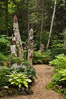 Chemin de paillis de cèdre menant à travers un jardin boisé avec nichoirs sur betula - souches de bouleau, ptéridophyte - fougères et hostas, été