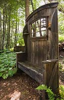 Ancien banc à dossier haut en bois avec cadre de fenêtre. Pteridophyta - fougères et pétasites japonicus - pétasite dans le jardin boisé, l'été