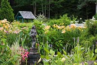 Fontaine d'eau à côté d'Impatiens roses et parterre de fleurs avec Hemerocallis rose et orange - Daylilies in backyard Country garden en été, Jardin des Mesanges garden, Québec, Canada