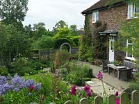 Cottage des années 1930 surplombant le jardin supérieur, séparé du jardin inférieur par une arche de moongate et d'if. Parterres d'aster, dahlia, gaura, boîte, géranium rustique, rose, verveine, salvia, sedum.