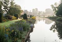 Le Long Pond avec la maison au-delà, bordé d'ifs coupés et le parterre de fleurs herbacées planté d'héléniums, kniphofias, dahlias, asters et eupatoriums. Forde Abbey, nr Chard, Dorset, Royaume-Uni