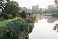 Le Long Pond avec maison au-delà, bordé par le parterre de fleurs herbacées planté d'héléniums, kniphofias, dahlias, asters et eupatoriums. Forde Abbey, nr Chard, Dorset, Royaume-Uni
