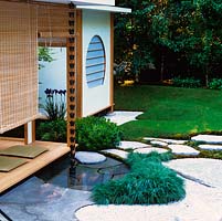 La véranda donne sur un paysage japonais naturel idéalisé de ruisseau sec, une piscine peu profonde alimentée par la chaîne de pluie du toit, des placages rocheux, un chemin en pierre et un bois.
