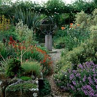 Chemin de gravier dans un jardin de style méditerranéen mène à la sphère armillaire et à la pergola. Parterres de Salvia lavandulifolia, pavot, phlome, yucca, iris barbu et helianthemum.
