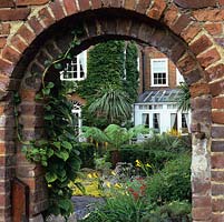 La porte dans le mur de briques géorgiennes donne un aperçu du jardin de la ville avec penstemon, géranium, fougères arborescentes, Jenny rampante, cordyline, palmier, lis du jour doré et ligularia.