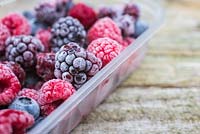 Fruits d'été congelés. Pot en plastique plein de baies fourragères congelées. Avec bleuets - Vaccinium, framboises et mûres - Rubus fruticosus