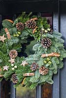Couronne de Noël décorée de pommes de pin, de boules, de bâtons de cannelle, de tranches d'orange et d'étoiles en bois fabriquées par Sue Wright. Veddw House Garden, Devauden, Monmouthshire, Pays de Galles