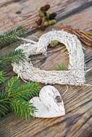 Un cœur blanc sur une surface en bois, accompagné d'un cœur de bouleau, de feuillage de pin, de cônes d'aulne et de chatons