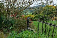 Une vue d'une statue entourée d'Euphorbia mellifera, fenouil et Rosa Hertfordshire. Au-delà, un ruisseau mène l'œil à la vue de la vallée de l'Axe.
